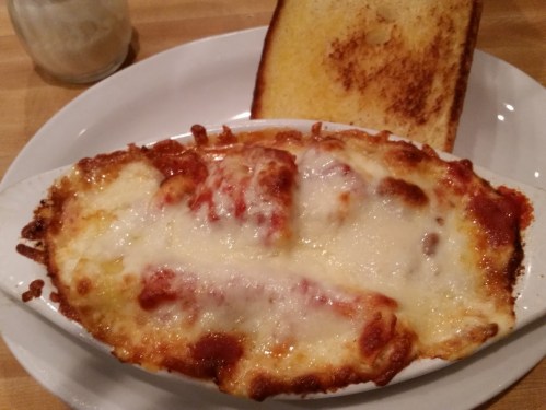A baked dish of cheesy lasagna with marinara sauce, served alongside a slice of toasted bread.