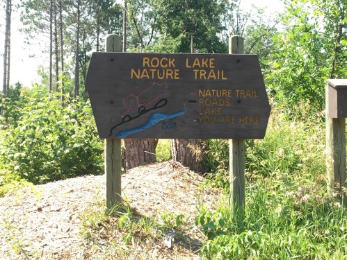 Wooden sign for Rock Lake Nature Trail, indicating nature trail, roads, and location with "You Are Here" marker.