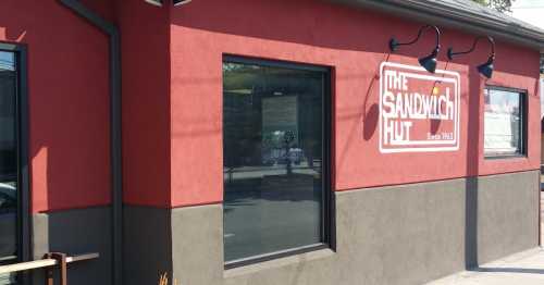 Exterior of The Sandwich Hut, featuring a red wall, large window, and a sign that reads "Since 1963."