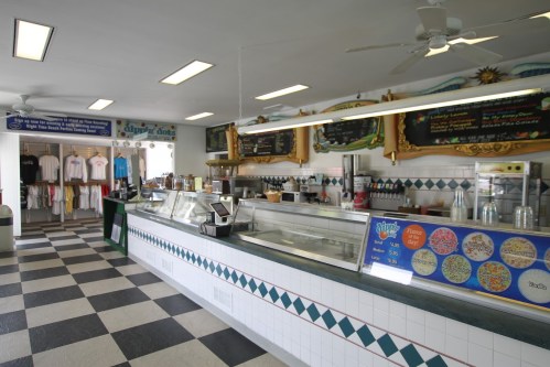 Interior of an ice cream shop featuring a service counter, menu board, and merchandise display with checkered flooring.