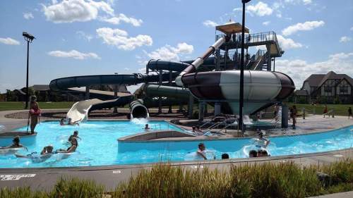 A water park featuring multiple slides and a pool, with people enjoying the water on a sunny day.