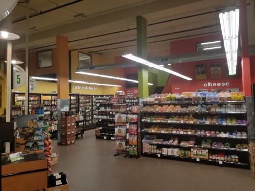 A grocery store interior featuring shelves of snacks, wine, beer, and cheese in a colorful setting.