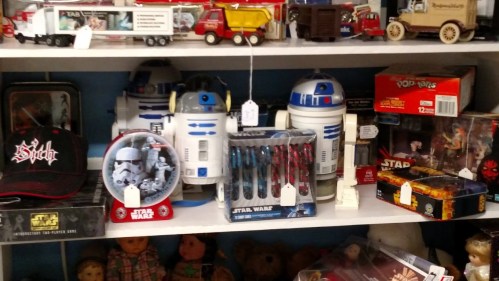 A shelf filled with various Star Wars collectibles, including R2-D2 figures, toys, pens, and a hat.
