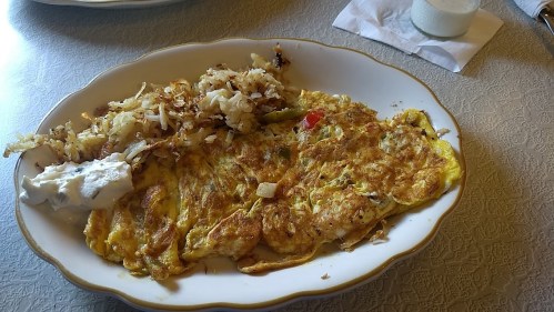 A plate of omelette with vegetables, served alongside crispy hash browns and a dollop of sour cream.
