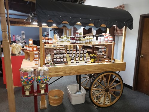 A wooden cart filled with jars of preserves and candies, featuring a canopy and two gumball machines on the side.