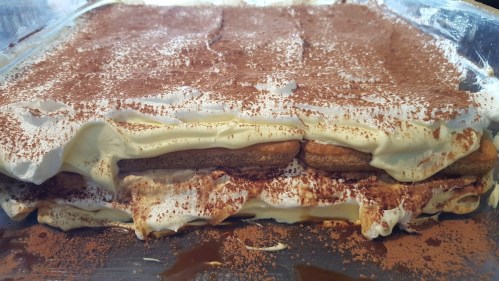 A close-up of a layered dessert with cream, cookies, and cocoa powder on top, in a clear dish.