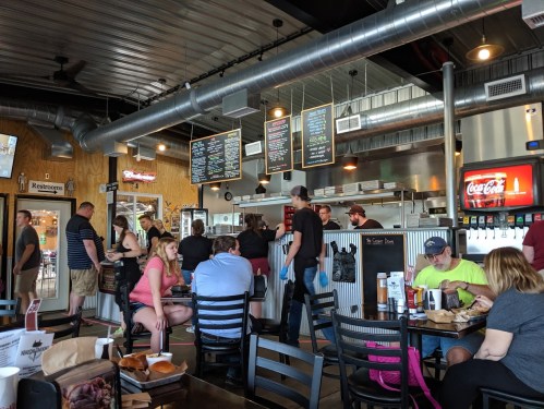A busy restaurant interior with customers ordering at the counter and others dining at tables.