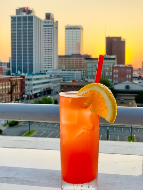 A refreshing cocktail with a slice of orange, set against a sunset skyline of a city.