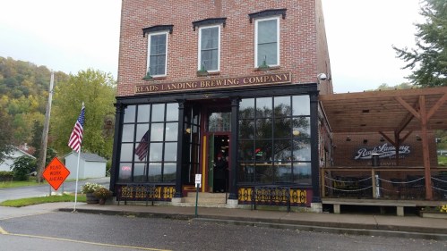 Exterior of Reads Landing Brewing Company, featuring large windows, an American flag, and autumn foliage in the background.