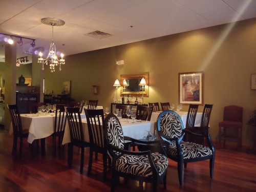Elegant restaurant interior with wooden floors, white tablecloths, and zebra-patterned chairs under soft lighting.