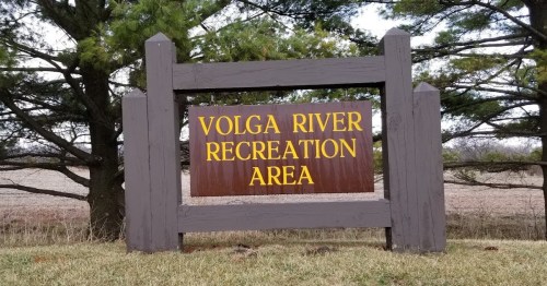 Sign for Volga River Recreation Area, featuring brown background with yellow text, surrounded by trees and grass.
