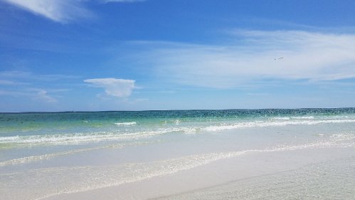 A serene beach scene with gentle waves, clear blue skies, and a calm ocean stretching to the horizon.