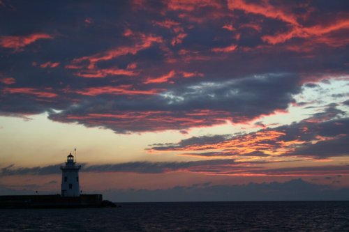A lighthouse silhouetted against a vibrant sunset with colorful clouds over the ocean.