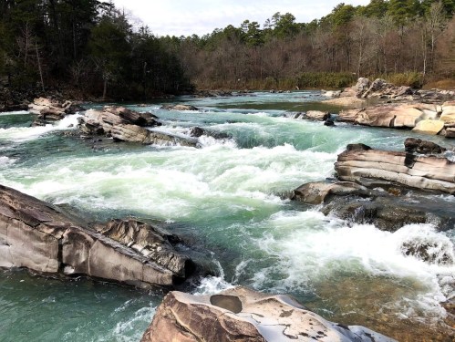 A flowing river with rocky banks, surrounded by trees and a serene natural landscape.