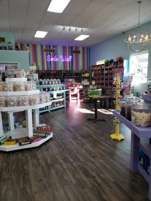 Brightly colored candy store interior featuring a "Soda Wall," shelves of sweets, and a cozy seating area.