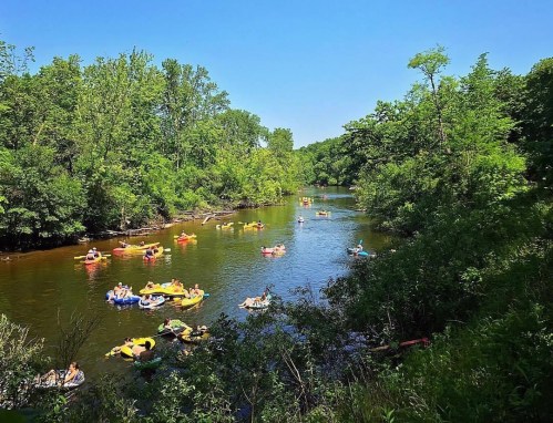A scenic river with people floating on colorful rafts surrounded by lush green trees under a clear blue sky.