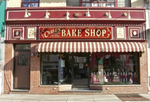 Exterior of Carlo's Bake Shop, featuring a red and white striped awning and decorative signage.
