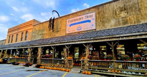 A rustic storefront with a sign reading "Dutchman's Store," decorated with pumpkins and flowers along the porch.