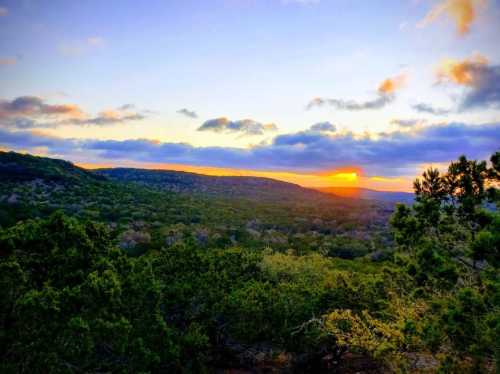 A vibrant sunset over rolling hills, with lush greenery in the foreground and colorful clouds in the sky.