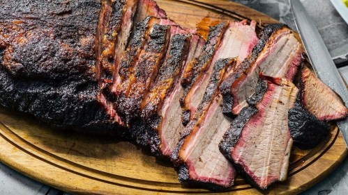 Sliced smoked brisket on a wooden platter, showcasing a smoky crust and tender pink interior.