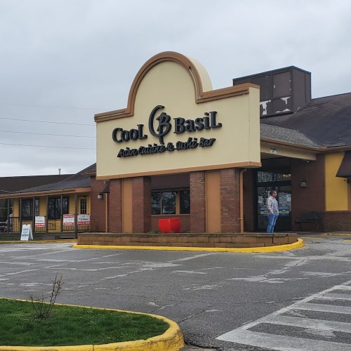Exterior of Cool Basil restaurant with a large sign, featuring a person standing near the entrance on a cloudy day.