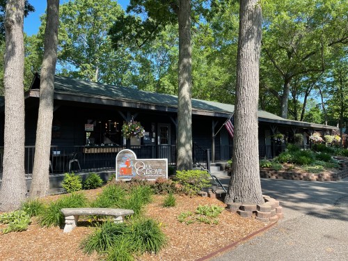 A charming black wooden building surrounded by trees and flowers, featuring a sign that reads "The Grove."