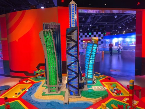 A colorful LEGO cityscape featuring tall buildings and a river, set in a vibrant play area.