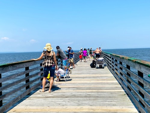 A busy fishing pier with people enjoying the day, some sitting on chairs and others fishing along the water.