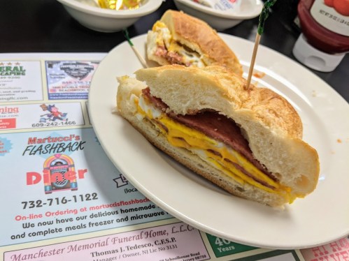 A close-up of a sandwich with layers of egg, ham, and cheese on a plate, with a toothpick holding it together.
