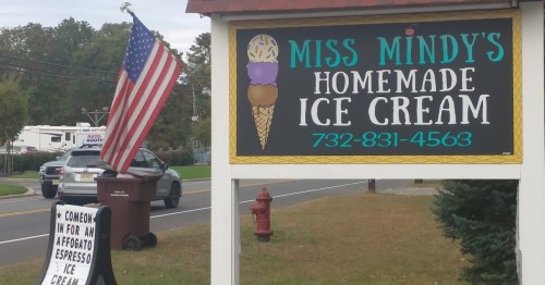 Sign for "Miss Mindy's Homemade Ice Cream" with an American flag, featuring an ice cream cone graphic and contact number.