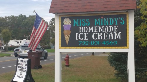 Sign for "Miss Mindy's Homemade Ice Cream" with an ice cream cone graphic and an American flag nearby.