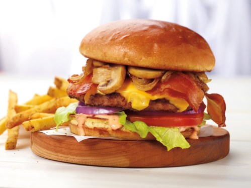 A juicy burger with bacon, cheese, mushrooms, lettuce, tomato, and onion, served with crispy fries on the side.