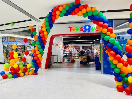 Colorful balloon archway leading to a Toys"R" Us store entrance, showcasing a vibrant and inviting atmosphere.