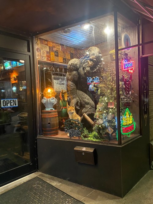 A storefront window display featuring a large bear statue, neon signs, and various decorative items.
