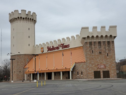 Exterior of a Medieval Times venue featuring a castle-like structure with a tower and striped awnings.