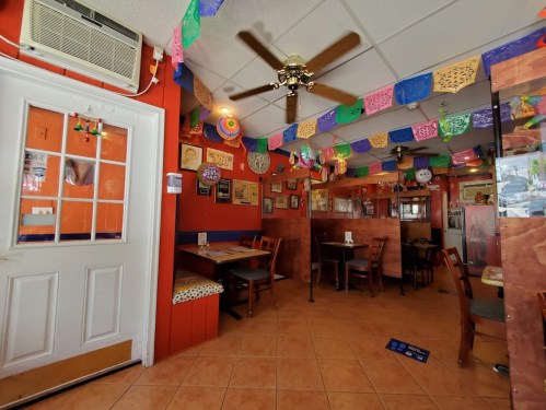 Cozy restaurant interior with colorful papel picado decorations, wooden tables, and a ceiling fan.