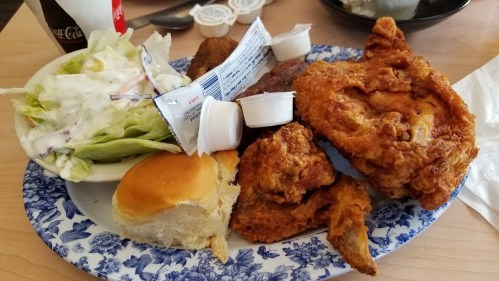 A plate of fried chicken, a biscuit, salad, and dipping sauces on a floral-patterned plate.