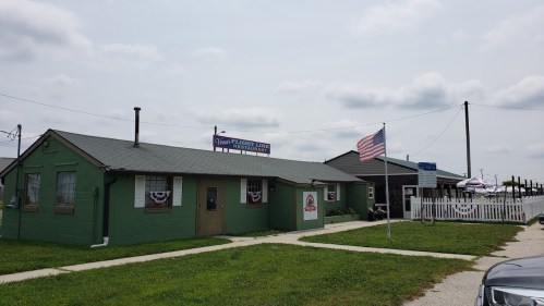 A green building with a sign reading "Pleasant Lake Festival" and an American flag, set against a cloudy sky.