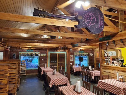 Cozy restaurant interior with wooden beams, checkered tablecloths, and a guitar hanging from the ceiling.