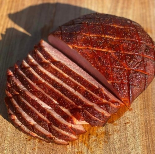 Sliced smoked ham on a wooden cutting board, showcasing a crispy, caramelized exterior and tender pink interior.