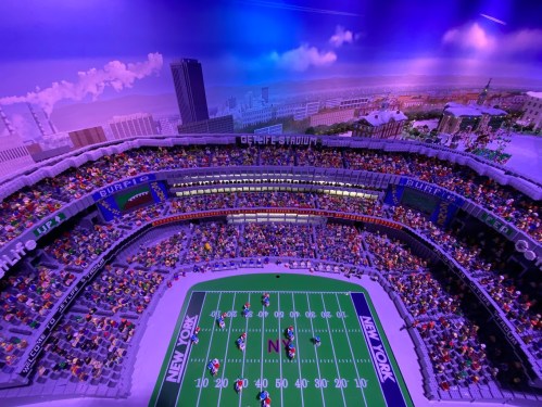 Aerial view of a vibrant stadium filled with fans, featuring a football field and city skyline in the background.