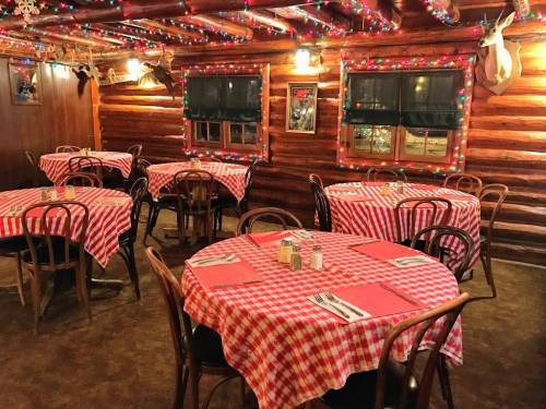 Cozy restaurant interior with wooden walls, red and white checkered tables, and festive lights.