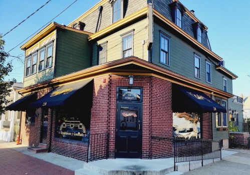 A corner restaurant with a green and brick exterior, featuring outdoor seating and awnings.