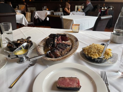 A table set in a restaurant featuring a platter of steak, sides of macaroni and mushrooms, and a slice of beef.
