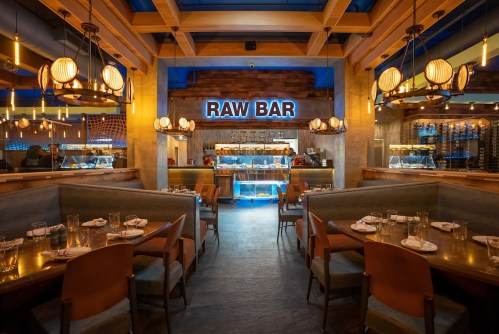 Interior of a modern restaurant featuring a raw bar, with wooden decor, ambient lighting, and cozy seating arrangements.