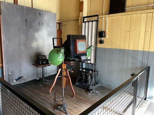 A vintage photography setup featuring a large camera, green lamps, and various equipment in a wooden room.