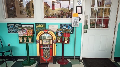 A colorful jukebox and vintage candy machines near a welcoming entrance in a retro-themed diner.