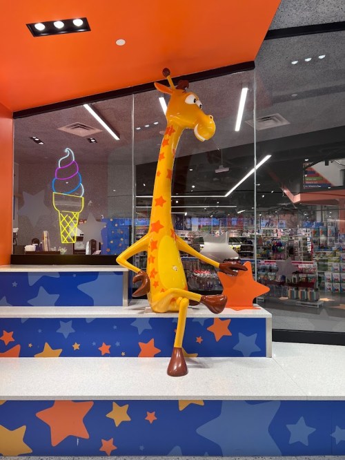 A cartoon giraffe statue sits on a colorful display in a store, with an ice cream sign in the background.