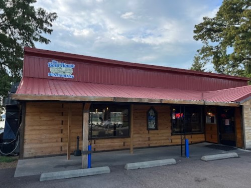 Exterior of a wooden restaurant with a red metal roof, featuring a sign that reads "The Boat House Restaurant."