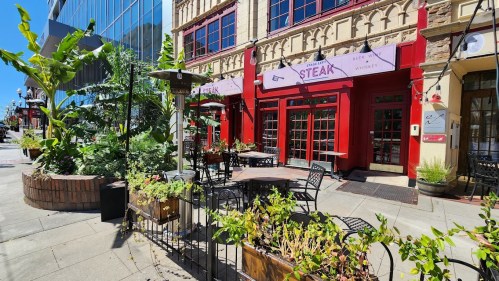 A vibrant restaurant exterior with red accents, outdoor seating, and greenery on a sunny day.